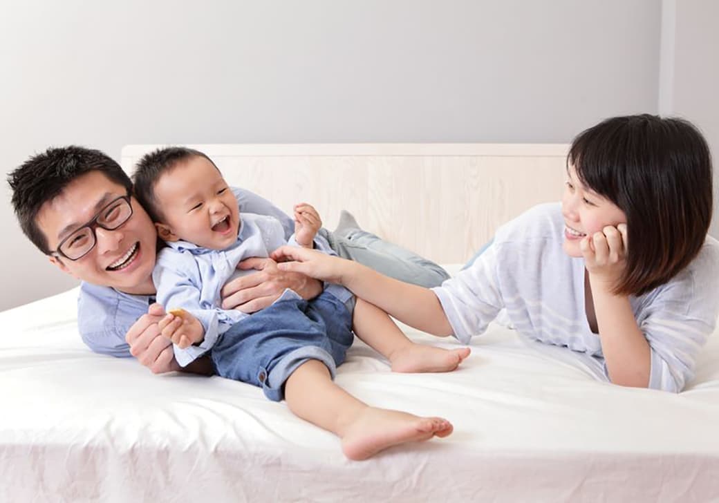 A mother and father playing with their child on a bed.