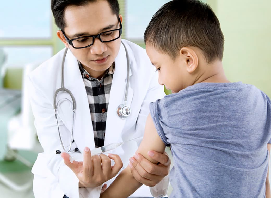 Male doctor administering flu shot to young boy in an office.